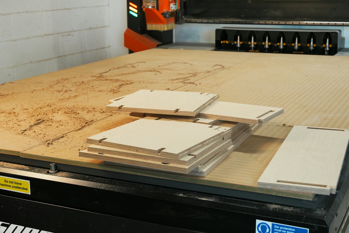 Fresadora CNC cortando madera contrachapada en un taller con polvo de madera.